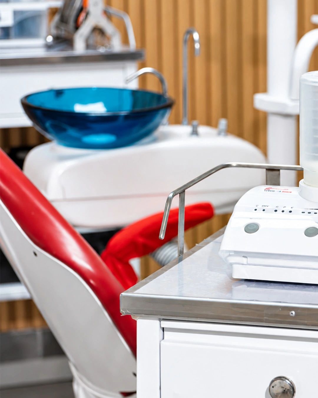 El sillón dental rojo y la escupidera azul del consultorio, frente a una pared revestida en madera