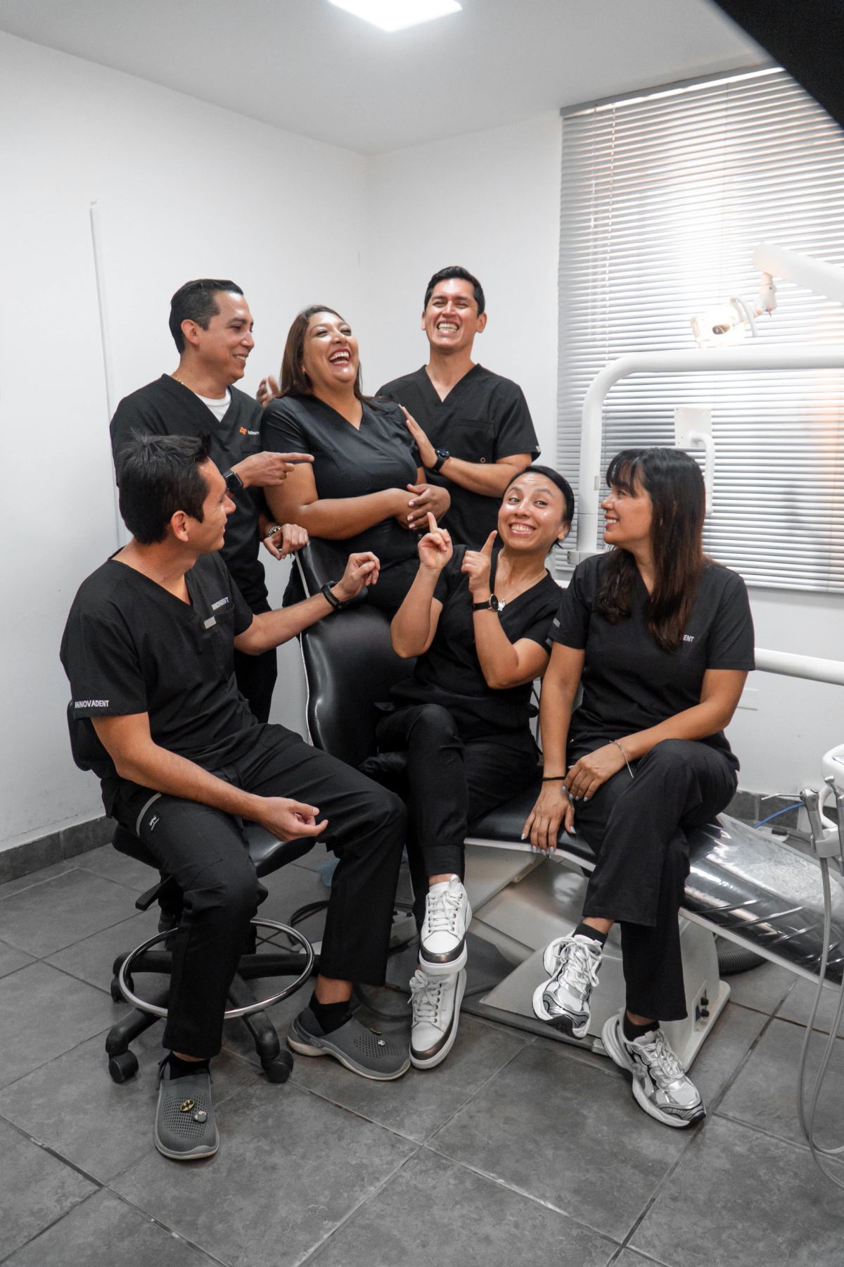 Seis integrantes del equipo de Innovadent con uniforme negro, riendo juntos alrededor de un sillón dental en una de las salas clínicas.