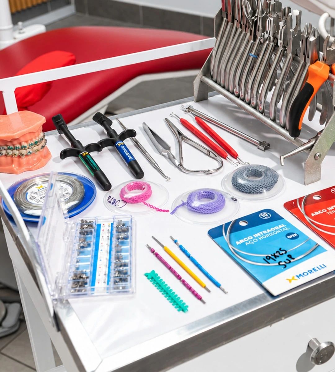 Una mesa con alicates de ortodoncia, arcos, brackets, ligaduras de colores y un modelo dental con brackets