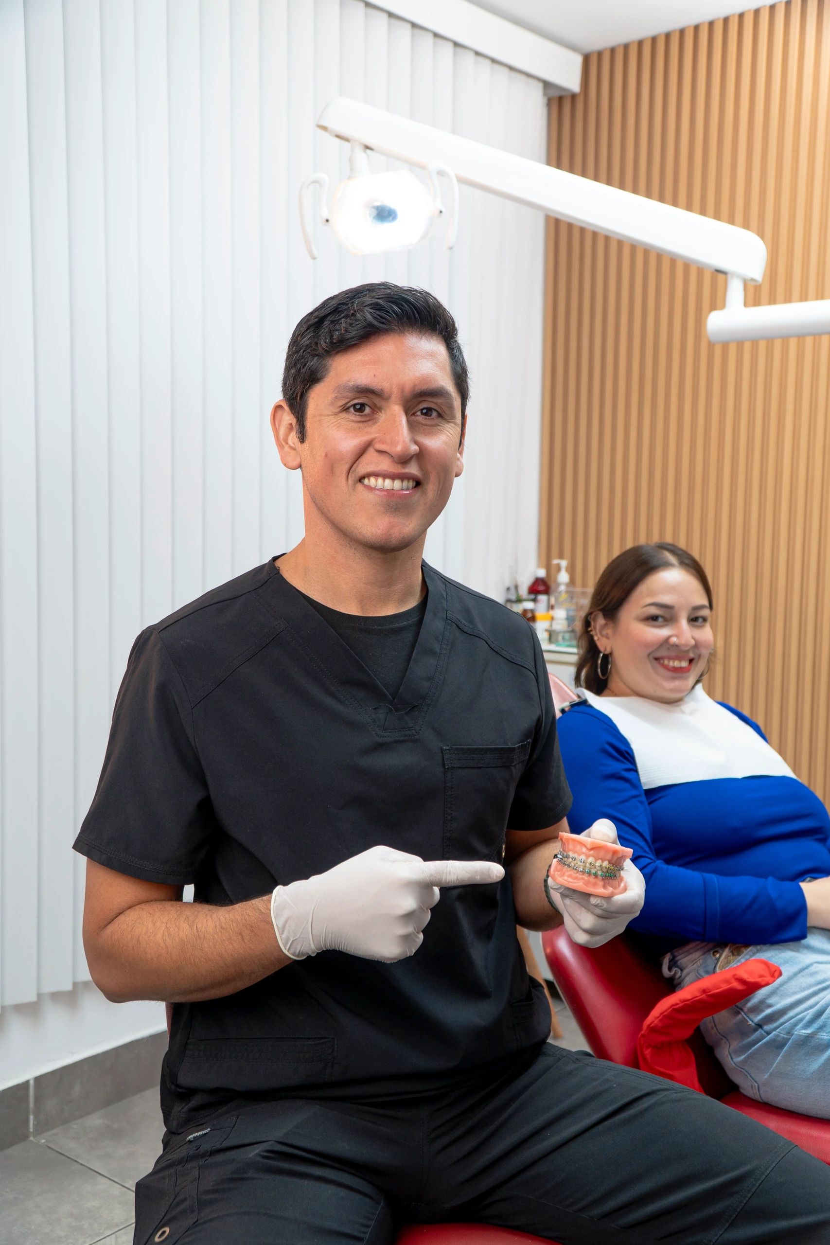 El especialista señala un modelo dental con brackets mientras la paciente sonríe sentada en el sillón.