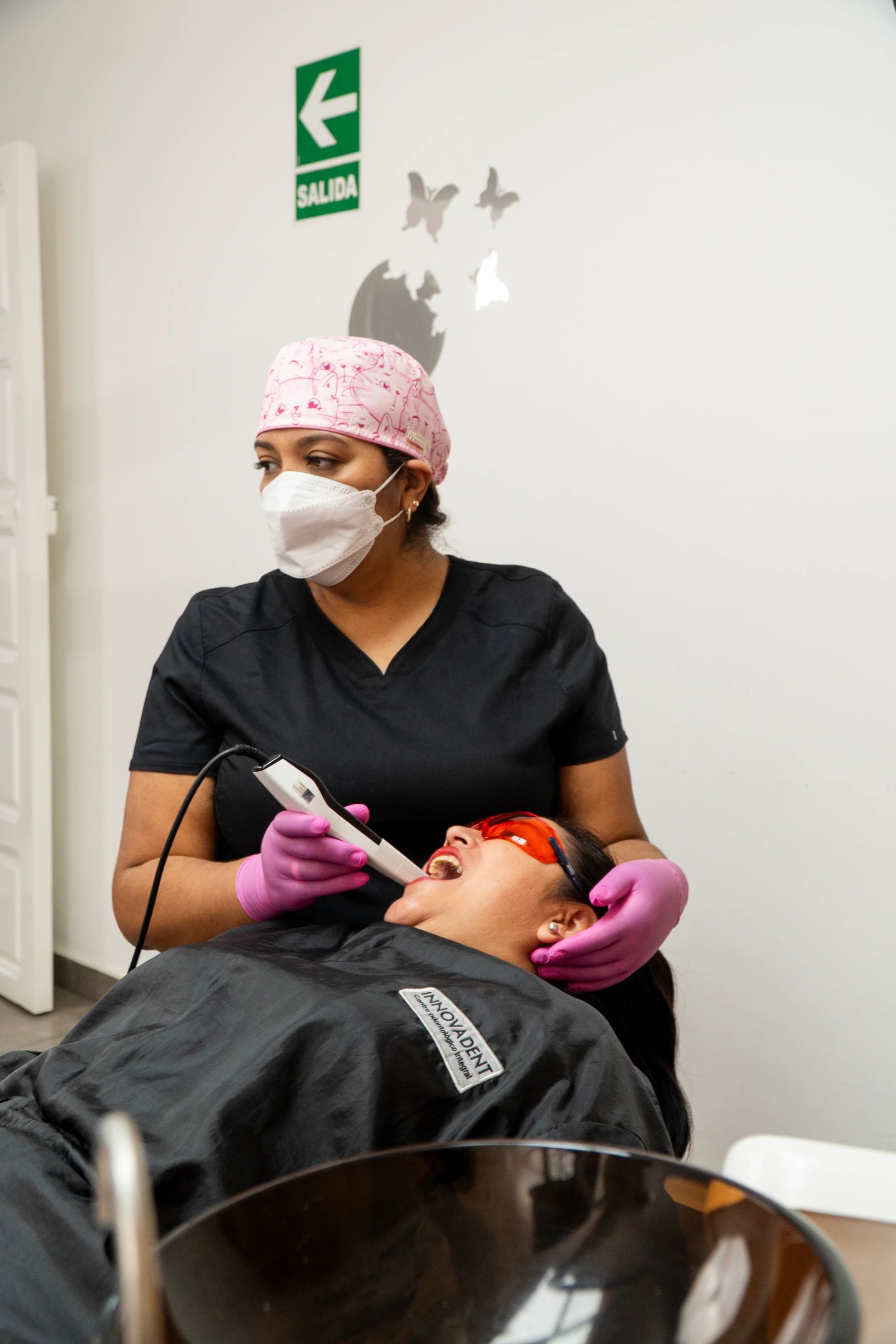 La especialista recorre con la cámara intraoral la boca de la paciente, recostada en el sillón con lentes de protección.